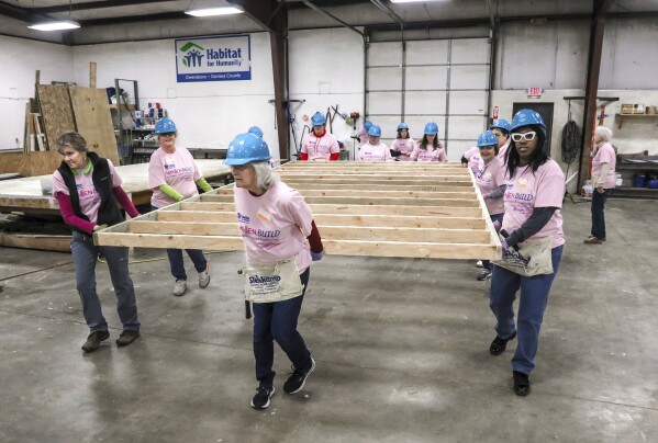 Volunteers carry a newly-constructed wall section inside the Habitat for Humanity Owensboro's indoor workshop, Jan. 13, 2024, in Owensboro, Ky. (Greg Eans/The Messenger-Inquirer via AP, File)